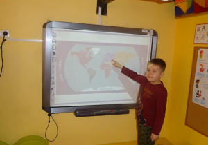 Chłopiec stoi pod tablicą interaktywną i wskazuje na mapie Polskę.